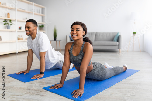 Cool black couple doing cobra pose on yoga mat in living room. Stay home activities concept