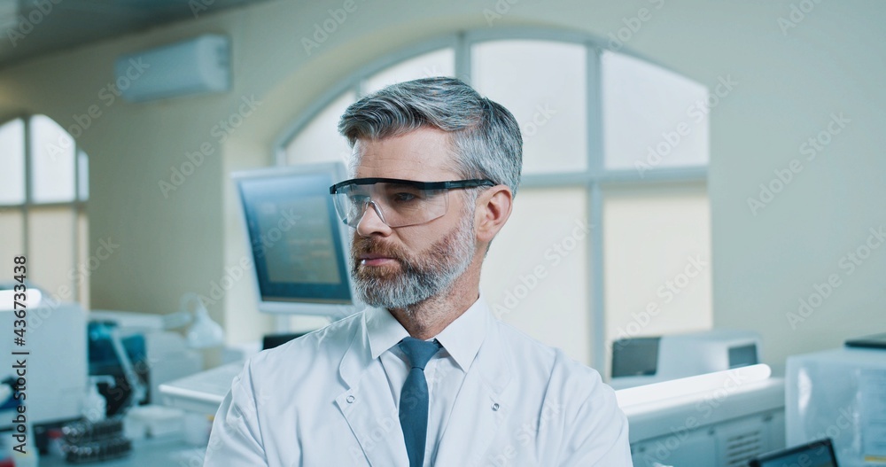 Close up portrait of Caucasian bearded middle-aged male doctor standing in clinic laboratory looking at camera and smiling. Handsome happy man lab specialist at workplace in hospital. Medic concept Close up portrait of Caucasian bearded middle-aged male doctor standing in clinic laboratory looking at camera and smiling. Handsome happy man lab specialist at workplace in hospital. Medic concept