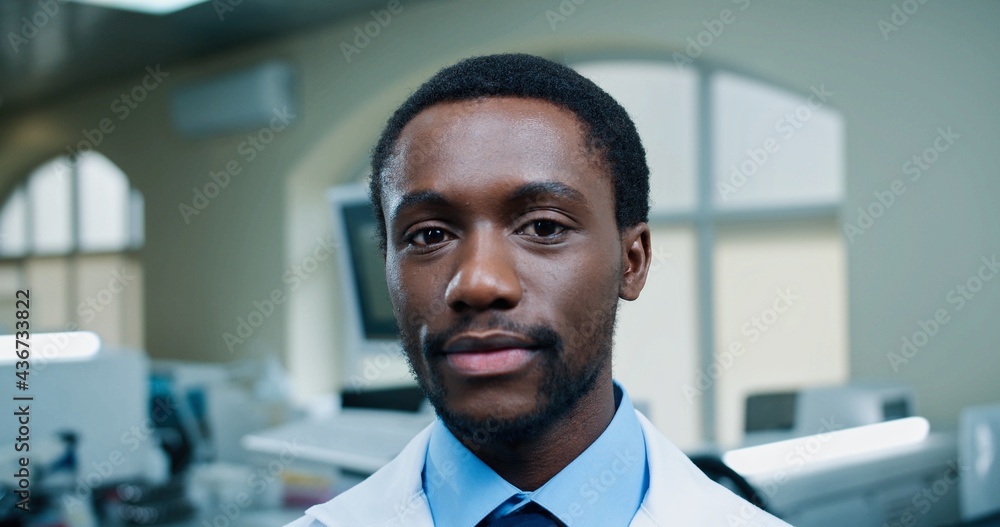 Obraz premium Close up portrait of happy positive African AMerican young man doctor in hospital looking at camera and smiling in good mood. Medicine, medical worker, young specialist in clinic, medic concept