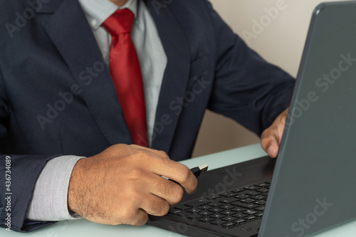 man in front of a computer and holding on a pen drive under the white table