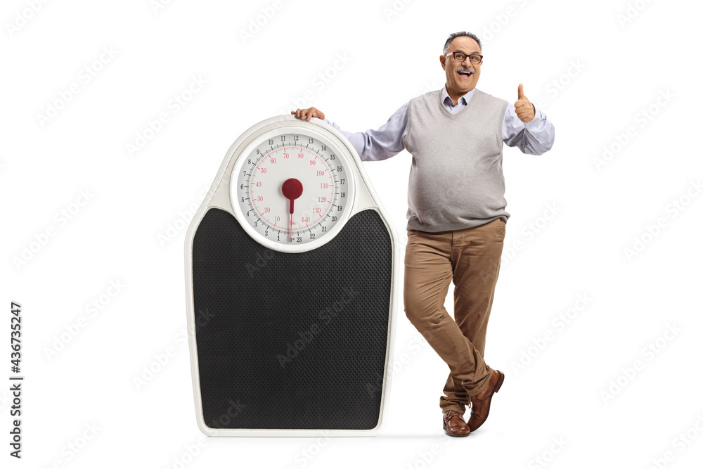Full length portrait of a mature corpulent man leaning on a big scale and showing thumbs up - obrazy, fototapety, plakaty 