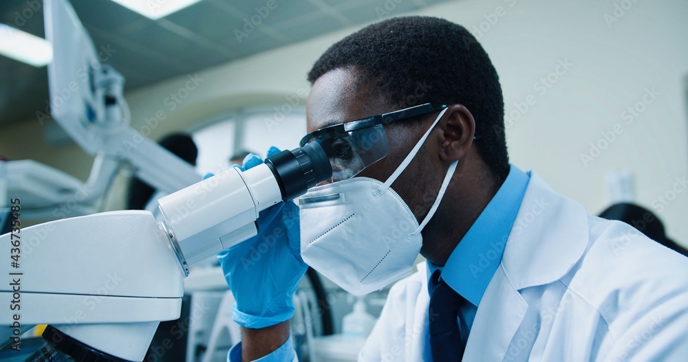 Close up of African American young male medical scientist working in  laboratory on coronavirus cure. Man doctor in mask looking at blood cells  analysis through microscope, experiment concept Stock Photo | Adobe