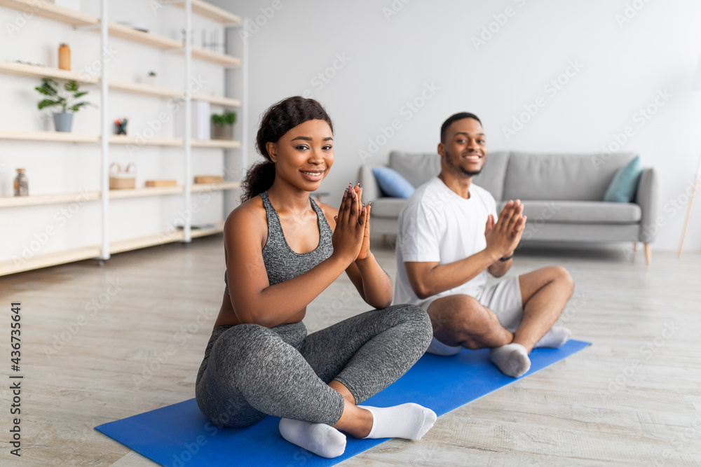 Home yoga practice during covid. Black couple meditating or doing breathing exercises, sitting in lotus pose at home Home yoga practice during covid. Black couple meditating or doing breathing exercises, sitting in lotus pose at home