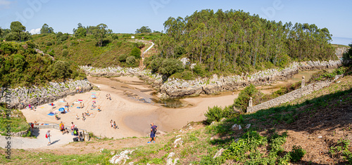 Vistas panorámicas de gente tomando el sol en la Playa de Guadamia, rodeada de vegetación verde, en las vacaciones de verano de 2020 en Asturias, norte de España. photo