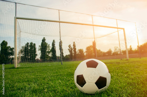 Soccer ball on a green grass field on sunset in front of goal 