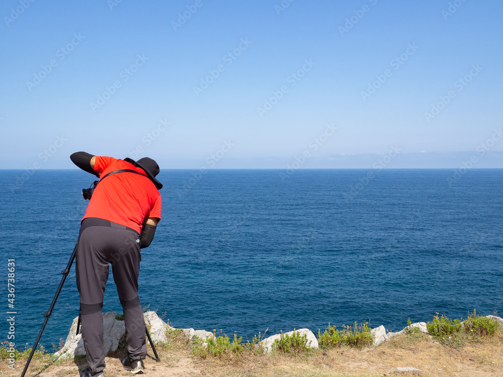 Persona fotgrafiando las vistas de la costa de Asturias en España, desde los Bufones de Prias, con paisaje rocoso, y aguas azules, en las vacaciones de verano de 2020