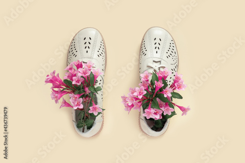 Pale white female shoes decorated with pink weigela on yellow background. Flat lay, top view trendy fashion feminine background.