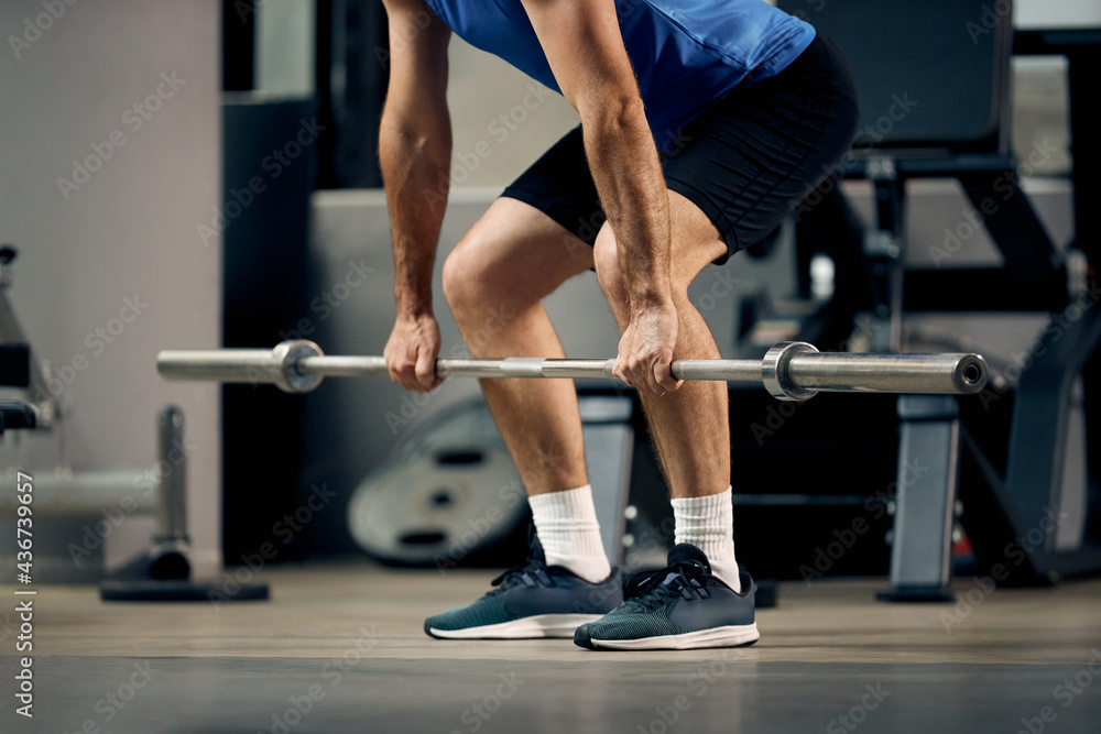 Unrecognizable mature sportsman exercising with barbell during strength training in gym. Unrecognizable mature sportsman exercising with barbell during strength training in gym.