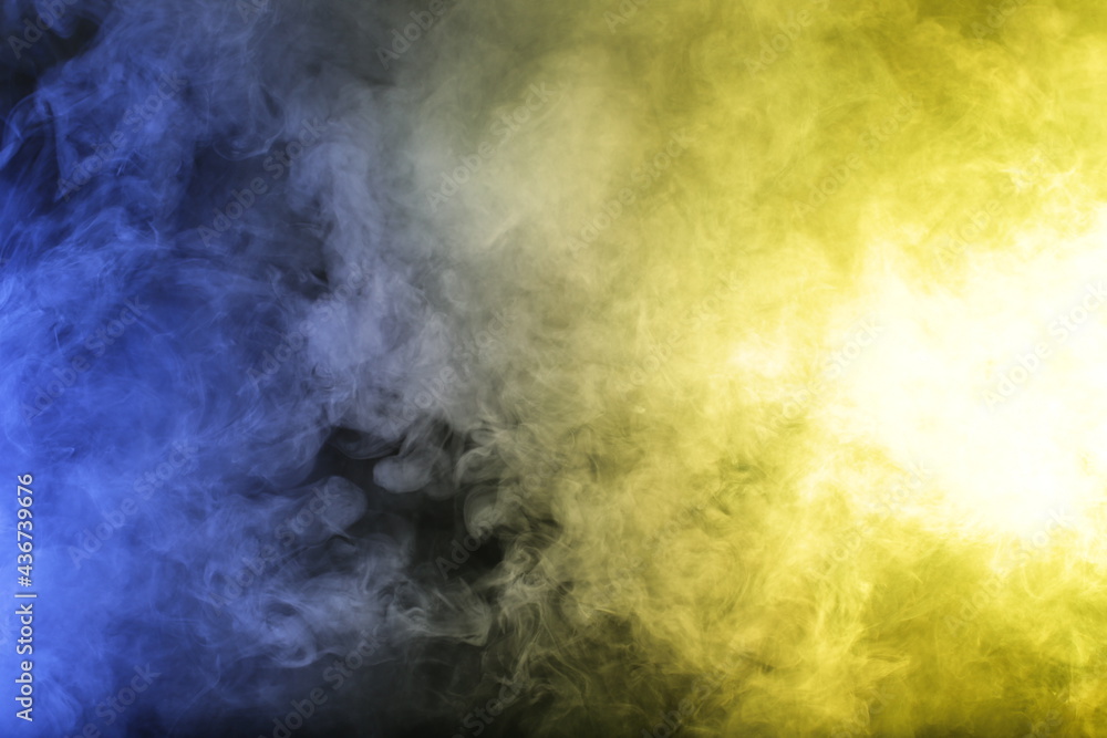 Artificial magic smoke in blue yellow light on black background