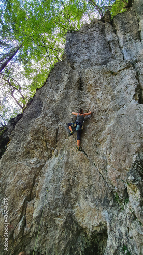 VERTICAL: Female rock climber scales a steep wall with top rope technique.