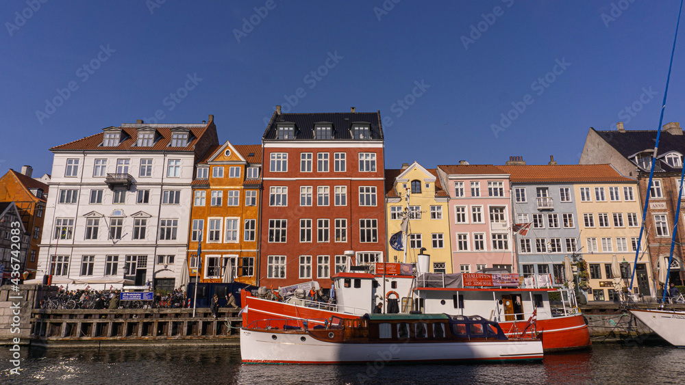 Calle Nyhavn en Copenague donde se ve el rio y una barca con el cielo azul