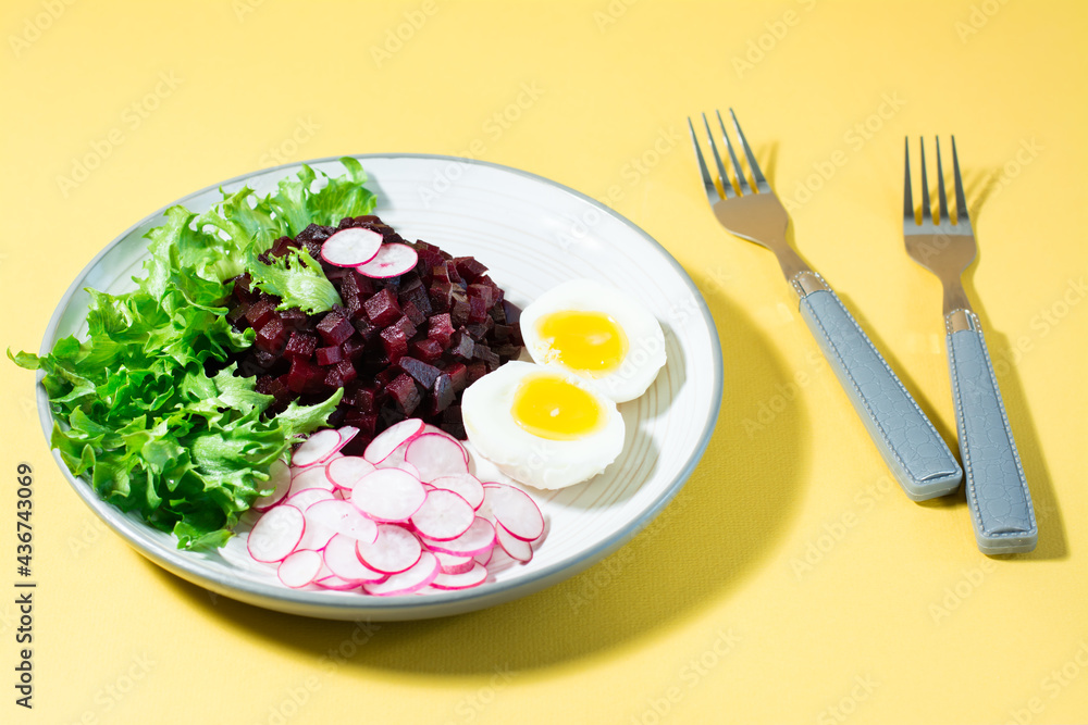 A dietary dish made from vegetables. Beet tartare, radish, frisee salad and boiled egg on a plate and a fork on a yellow background. Hard light A dietary dish made from vegetables. Beet tartare, radish, frisee salad and boiled egg on a plate and a fork on a yellow background. Hard light