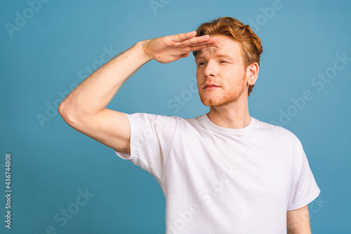 Portrait of a serious young man straring and looking far away isolated on blue background.