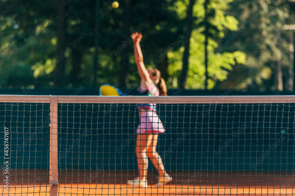 Pretty female tennis player observed through the net.