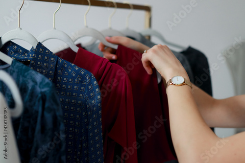Young woman personal stylist goes through hangers with clothes close up picking up outfit to wear