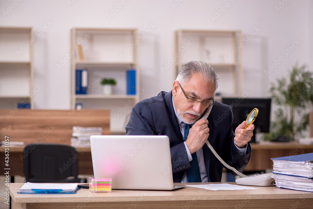 Old male employee auditor holding loupe at workplace Old male employee auditor holding loupe at workplace