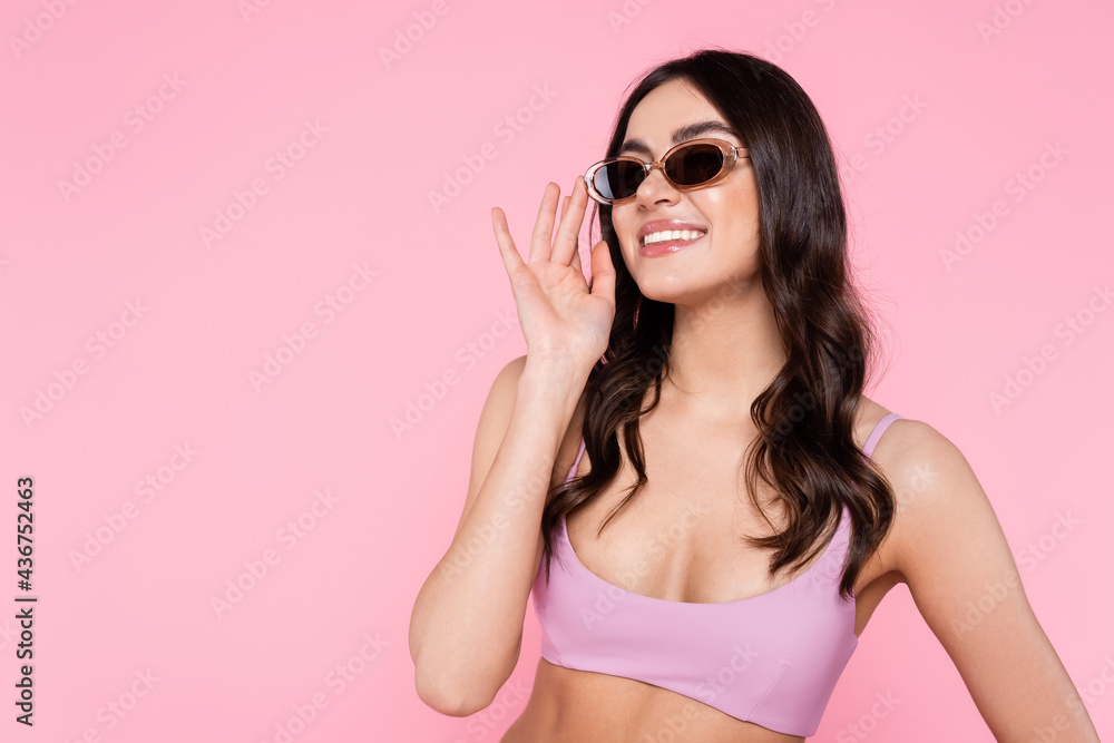 Smiling woman in sunglasses and top of swimsuit isolated on pink.