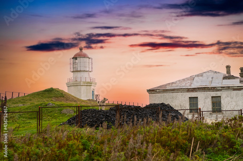 Landscape with an old lighthouse on the background of the sunset.
