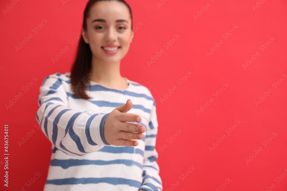 Happy young woman offering handshake against red background, focus on hand. Space for text Happy young woman offering handshake against red background, focus on hand. Space for text