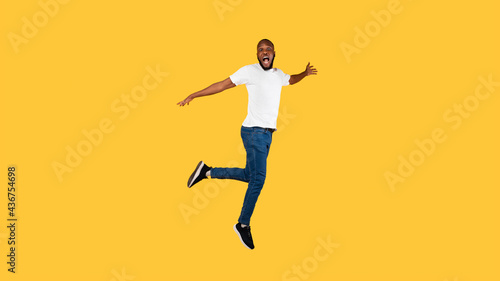 Shocked African American Guy Jumping Looking At Camera, Yellow Background © Prostock-studio