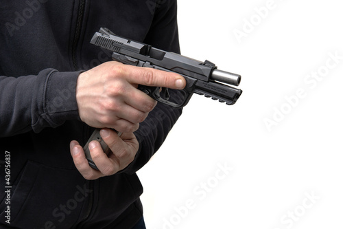 A man in dark clothes holds a pistol in his hands and reloads it. Unloaded weapon in hand.