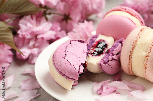 Delicious colorful macarons and pink flowers on grey table, closeup