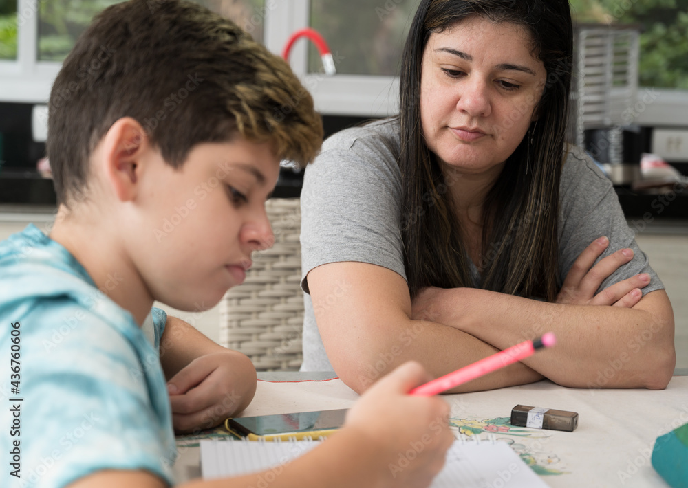 Mãe ajudando e orientando o filho estudante nas tarefas escolares dentro de casa. Dificuldades do ensino à distancia. Mãe ajudando e orientando o filho estudante nas tarefas escolares dentro de casa. Dificuldades do ensino à distancia.