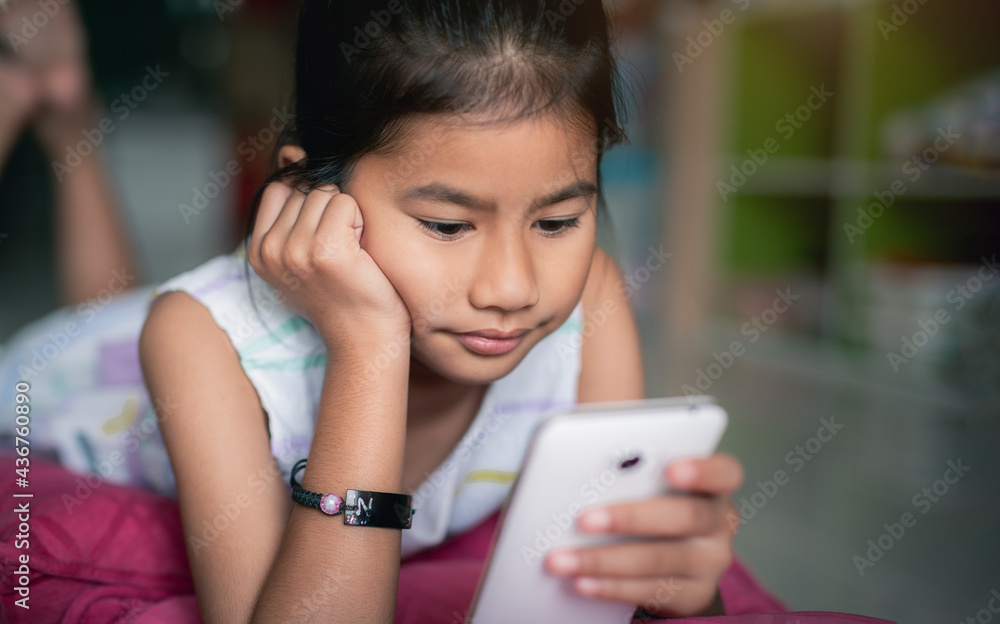 Teen Asian girl lying on carpet during watching video on smartphone in the home. Teen Asian girl lying on carpet during watching video on smartphone in the home.