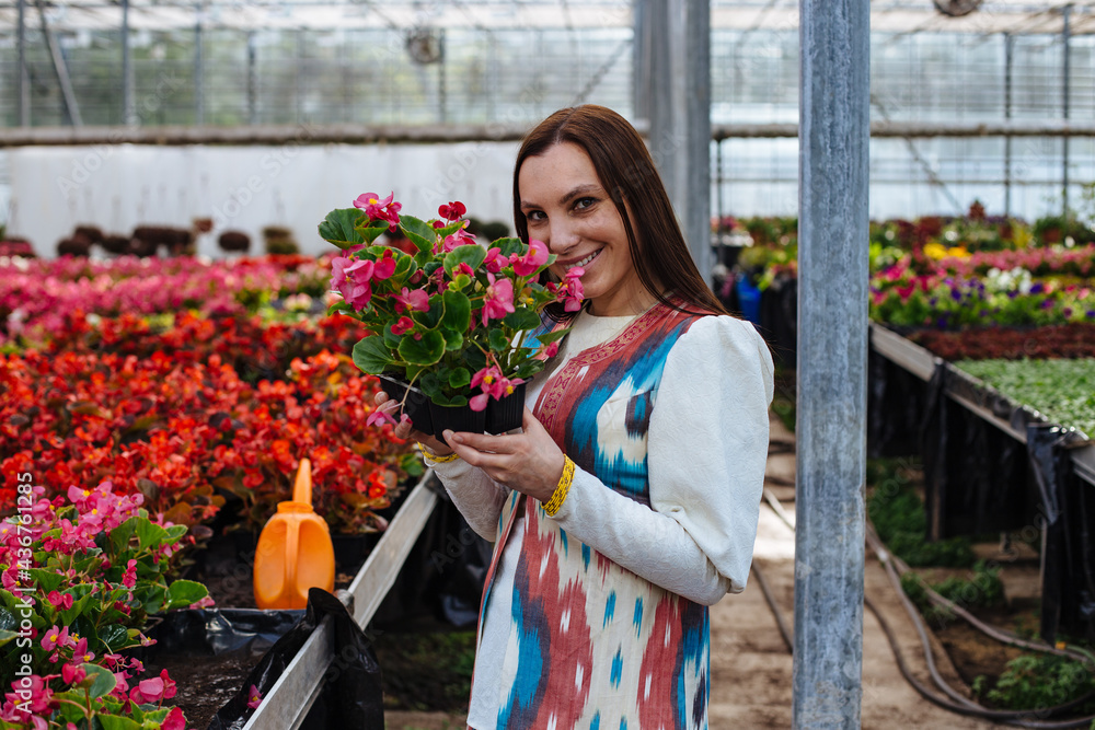 Attractive young woman with flowers in pot in greenhouse, gardening concept