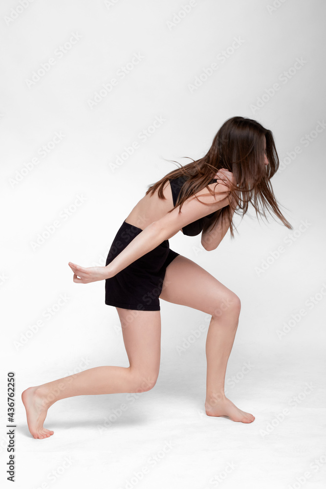 Young slim athletic girl, with long hair, in a black top and shorts, in the studio on a white background Young slim athletic girl, with long hair, in a black top and shorts, in the studio on a white background