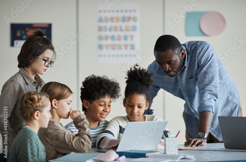 Wallpaper Mural Diverse group of children with male teacher using laptop together in modern scho