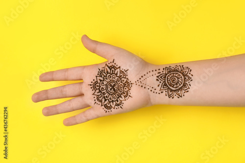Little girl with henna tattoo on palm against yellow background, closeup. Traditional mehndi ornament photo
