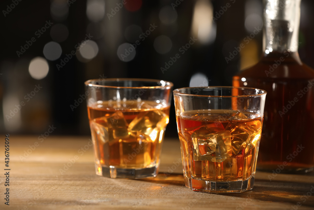 Glasses of whiskey with ice on wooden table in bar, space for text