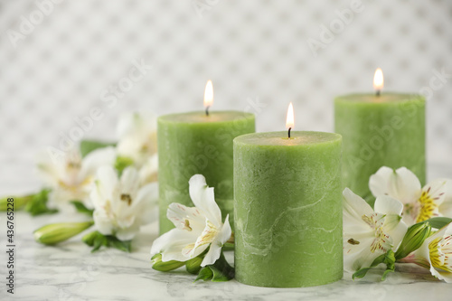 Burning candles and beautiful flowers on white marble table