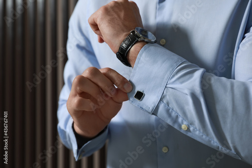 Stylish man putting on cufflink near wooden wall  closeup