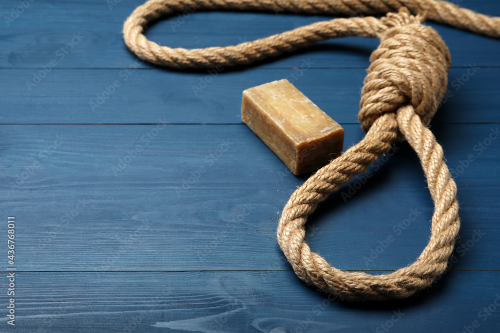 Rope noose and soap bar on blue wooden table. Space for text