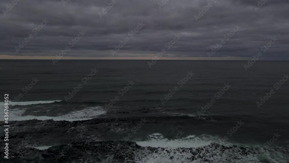 Drone shot flying backwards over a lighthouse on a moody dramatic morning or evening overlooking the ocean