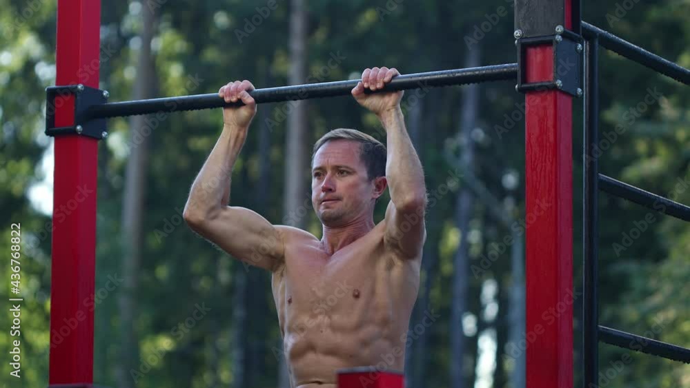 Workout in the park. Young caucasian man with lean body works out in the park and performs ABS exercises on the bar. Male with six pack works out outdoor Workout in the park. Young caucasian man with lean body works out in the park and performs ABS exercises on the bar. Male with six pack works out outdoor