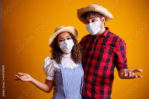 couple wearing typical clothes for the Festa Junina (Junina Party) and protection mask to prevent COVID-19. With open arms representing welcome photo