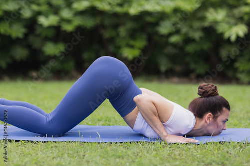 Portrait of happy young caucasian woman exercising yoga outdoors early morning. Beautiful girl practicing asana on blue yoga mat on green grass in park at summer © Алина Бузунова