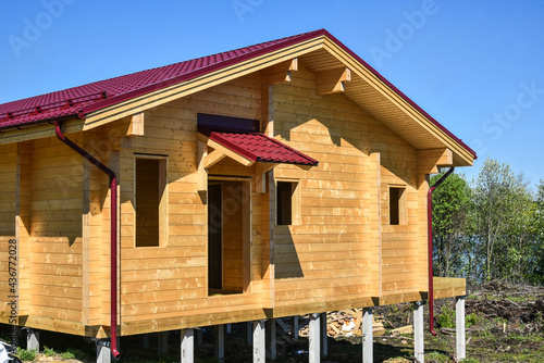 Ecological material. Country private house. One-storey timber house with a red roof for a large family on blue sky. The construction of ecological wood homes. Mortgage, loan, dream house.