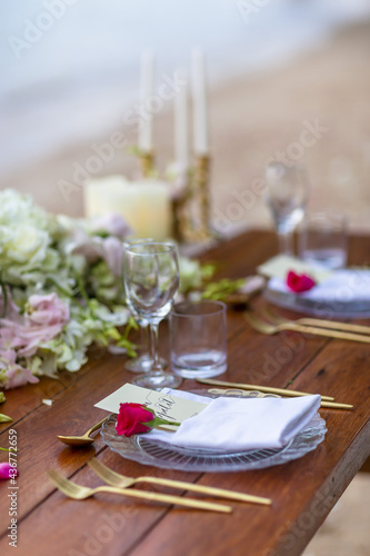 Romantic Wedding Table Top with Red Roses Layout Table Spread no people tropical beach location with gold cutlery and scenic view of sunset on the beach soft light © Huw Penson
