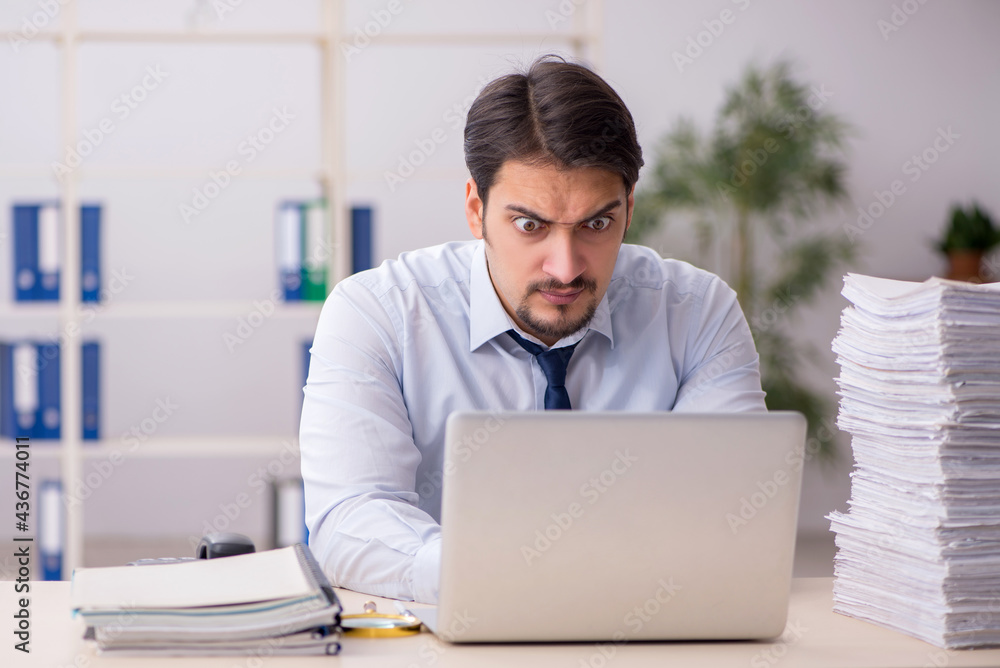 Fototapeta premium Young businessman employee unhappy with excessive work in the of