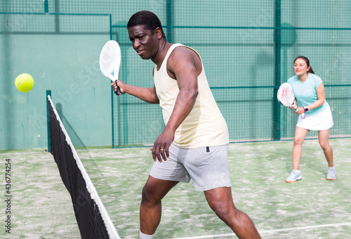 Young adult man playing doubles paddle tennis with female partner at warm sunny day, healthy lifestyle concept © JackF