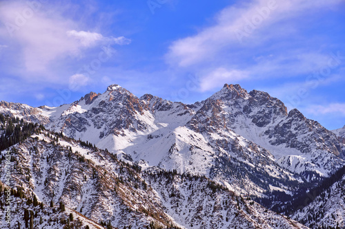 Majestic rocky peaks with fir forest on the background of blue sky with clouds in the winter season