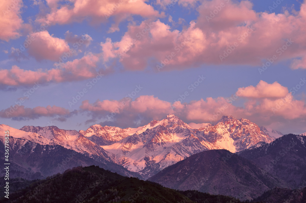 Majestic rocky peaks with fir forest on the background of  blue sky with clouds at sunset