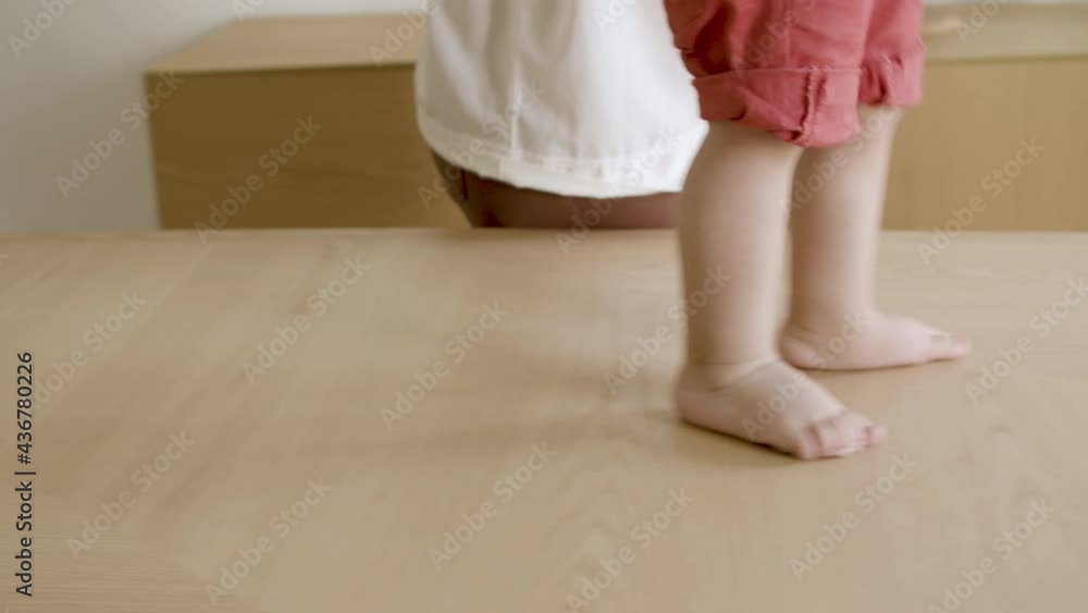 Close-up of barefoot little boys legs walking on table. Son doing his first steps at home with mothers help. First steps, parenthood, development concept. Close-up of barefoot little boys legs walking on table. Son doing his first steps at home with mothers help. First steps, parenthood, development concept.