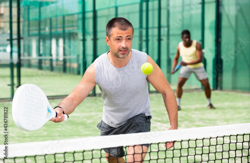 Athletic mens plays padel. View through the tennis net © JackF