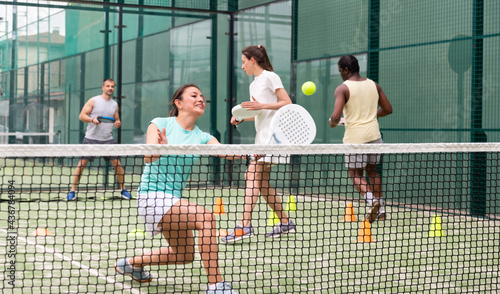 Portrait of cheerful woman paddle tennis player performing strokes technique at group training at court © JackF
