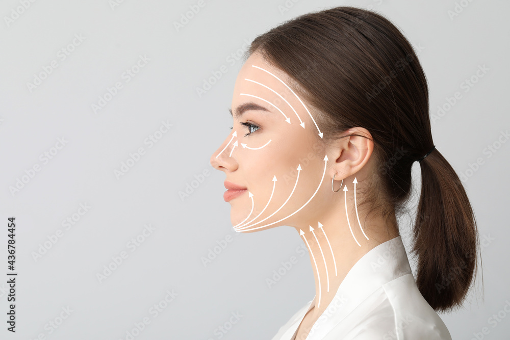 Young woman with arrows for massaging on her face against light background - obrazy, fototapety, plakaty 